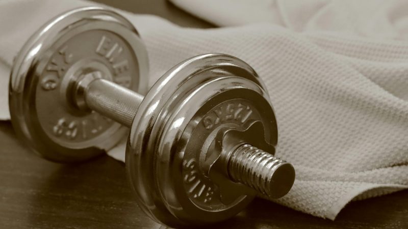 Chrome dumbbell and towel on dark wood.